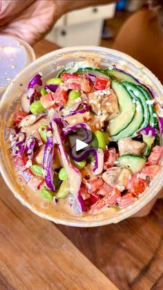 a bowl filled with lots of food sitting on top of a wooden table next to a person