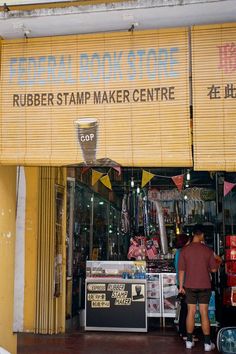 a man standing in front of a book store next to a yellow awning with the words rubber stamp maker centre on it