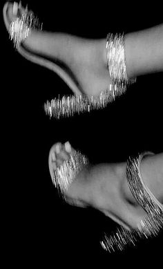 two women's feet with shiny silver sandals on top of each other and one has her foot in the air