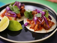 two tacos on a plate with lime and cilantro