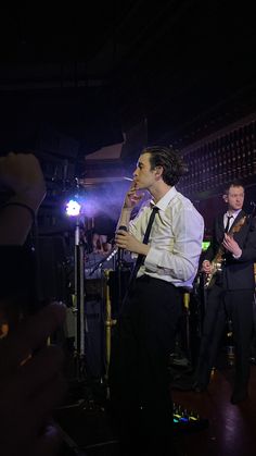 two men in suits and ties singing into microphones while another man plays the guitar