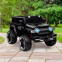 a black toy truck with lights on parked in front of a tree and grass area