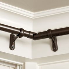 a close up of a metal curtain rod on a white wall with wood trimmings