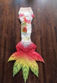 a mermaid tail made out of plastic on a wooden floor next to a vase with flowers