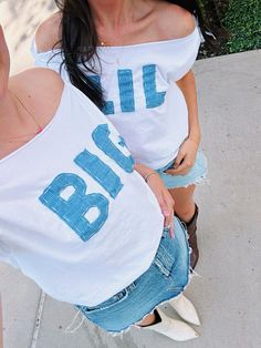 two women in white shirts are standing on the sidewalk