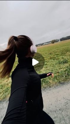 a woman with headphones is running in the grass and has her hair blowing in the wind