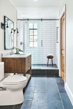 a white toilet sitting next to a walk in shower under a bathroom mirror on top of a wooden cabinet