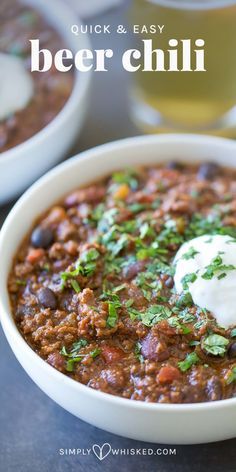 a bowl of chili with sour cream on top and two glasses of beer in the background