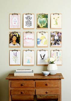 a wooden dresser sitting next to a wall with pictures on the wall and flowers in a vase