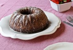 a bundt cake sitting on top of a white plate next to a bowl of strawberries