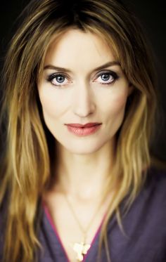 a woman with long hair and blue eyes is posing for a studio photo in front of a black background