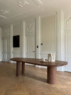 a wooden table sitting on top of a hard wood floor next to white wall panels