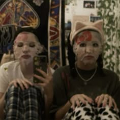 two girls with cat face paint on their faces and one girl is holding a cell phone