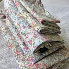 a pile of folded fabric sitting on top of a white bed covered in pink and blue flowers