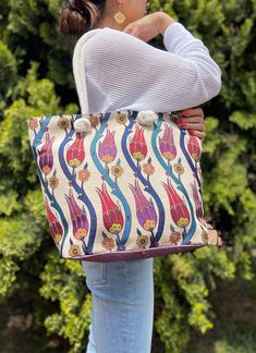 a woman carrying a colorful handbag in front of some bushes