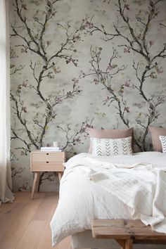 a bed sitting under a window next to a wallpaper covered in flowers and branches