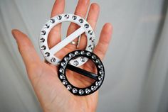 a hand holding a white and black peace sign brooch with crystal stones on it