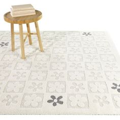 a white rug with flowers on it and a wooden stool in the middle next to it