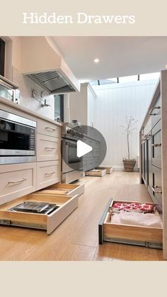 an open drawer in the middle of a kitchen with wooden flooring and white cabinets