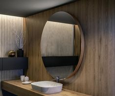 a bathroom with a large round mirror above the sink and wood paneling on the walls