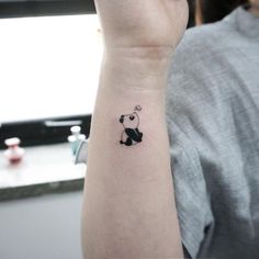 a small black and white panda bear tattoo on the left wrist, by a woman's arm