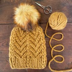 a knitted hat with two balls of yarn and a pair of scissors next to it