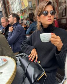 a woman sitting at an outdoor table holding a coffee cup