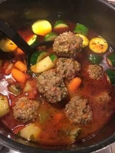 meatballs and vegetables are being cooked in a pot with a ladle on the stove