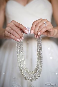 a woman in a wedding dress holding a necklace and diamond ring with her hands on it