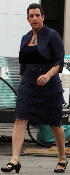 a woman in a dress and heels walking down the street with a man behind her