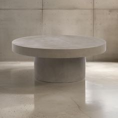 a round concrete table sitting on top of a cement floor next to a white wall