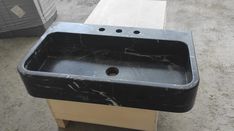 a black marble sink sitting on top of a wooden table next to a trash can