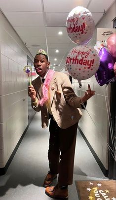 a young boy in a suit and tie holding some balloons with the words happy birthday on them