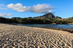 a sandy beach with mountains in the background and water on the other side that is surrounded by trees