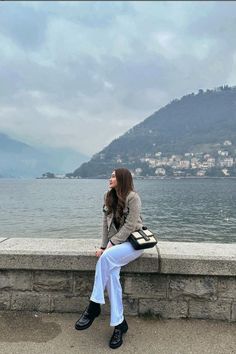 a woman is sitting on a ledge by the water