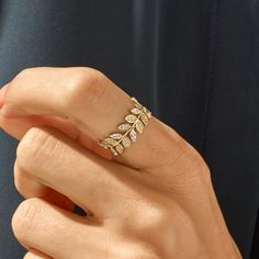 a woman's hand wearing a gold ring with leaves on the band and diamond accents