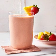 a smoothie in a glass with strawberries and pineapple on the side