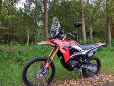 a red dirt bike parked on the side of a road in front of some trees