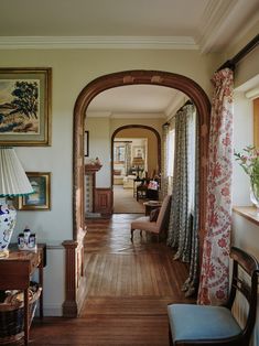 an archway leads into a living room with wood floors and curtains on the windowsill