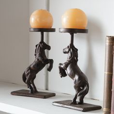 two horse figurines sitting on top of a white shelf next to a book