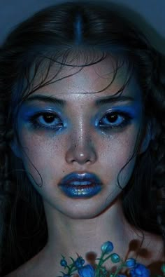 a woman with blue makeup and flowers on her neck is posing for a photo in the dark