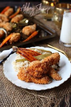 fried chicken and carrots on a plate next to some rice with a glass of milk in the background