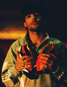 a man holding two pairs of shoes in his hands while wearing a hat and jacket