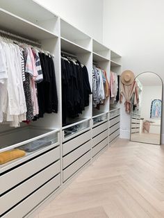 an organized closet with white drawers and clothes hanging on the wall, in front of a mirror