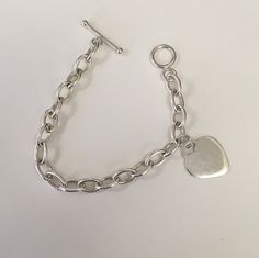 "Oval shaped large link chain in sterling silver with one heart charm.  Heart charm measures 24 mm tall and 0 mm wide.  The links measure 12 mm long by 7 mm wide and are solid.  The bracelet has a toggle clasp. The length of the bracelet is 7 1/2\".  This was preowned.  It is in good condition." Classic Silver Chain Charm Bracelet With Oval Links, Classic Silver Heart Bracelet, Classic Sterling Silver Charm Bracelet With Heart, Classic Sterling Silver Heart Charm Bracelet, Classic Silver Heart Bracelet With Lobster Clasp, Sterling Silver Charm Bracelet With Toggle Clasp, Minimalist Silver Chain Bracelet With Heart Charm, Classic Silver Heart Charm Bracelet, Personalized Silver Oval Link Chain Bracelet