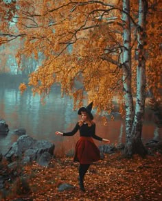 a woman in a black top and red skirt is standing near trees with yellow leaves