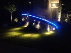 an illuminated bridge in the grass at night with blue light coming from it and some lights on