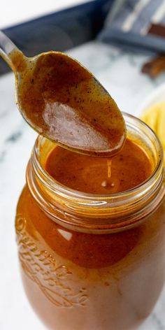 a spoon full of peanut butter sitting on top of a glass jar filled with liquid