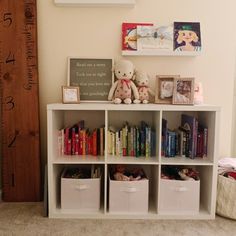 a white book shelf with books and stuffed animals on it next to a wall mounted clock