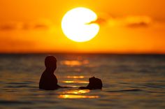 the sun is setting over the ocean with two people in the water looking at each other